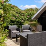 Terrasse mit drei Gartenstühlen und Tisch. Hintergrund: grüne Hecke mit rosa Blüten.