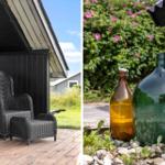Schwarzer Wicker-Sessel auf Terrasse. Große Glasbehälter im Garten mit rosa Blumen.