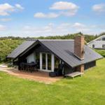 Moderne Villa mit Holzterrasse, Garten und Grillplatz unter blauem Himmel.