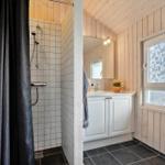 Badezimmer mit Dusche, Waschbecken und Toilette. Holzwände und Fenster mit Muster.