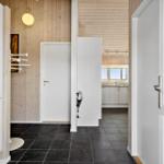 Hallenraum mit Holzwand, weißen Türen und dunklem Boden. Küche im Hintergrund sichtbar.