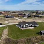 Haus mit Terrasse und Garten, umgeben von Grasland und weiteren Häusern in der Ferne.