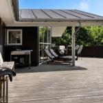 Terrasse mit Liegestühlen, Grill und Pflanzen. Holzdecke und Sicht auf Grün.