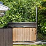 Hochwertiger Holzhot tub mit Edelstahlrohr auf Terrasse im Grünen.