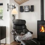 Ein schwarzes Ledersessel mit Felldecke steht vor einem Kamin mit brennendem Feuer.