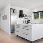 Moderne Küche mit weißer Arbeitsplatte, Edelstahl-Kühlschrank und Blick auf Wald.