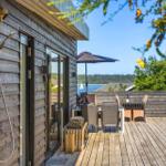 Terrasse mit Dusche an der Wand, Sitzgruppe und Blick auf Wasser.