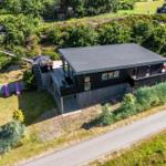 Moderne schwarze Hütte mit Terrasse, Garten und Waldumgebung.