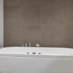 Eine weiße Badewanne mit Armlehnen und Duschkopf an der Wand