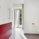 Badezimmer mit rotem Waschbeckenunterschrank, Spiegel und Tür zum Garten.