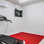 Fitnessraum mit Laufband und Dartboard auf rotem Boden