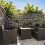 Terrasse mit Gartenmöbeln und Wicker-Zaun. Holzdecke und grüne Pflanzen im Hintergrund.