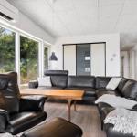 Wohnzimmer mit schwarzer Ledercouch, Holztisch und großem Fensterblick auf Grün.