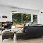 Wohnzimmer mit schwarzer Ledercouch, Sessel und Holztisch. Große Fenster und Glaswand.
