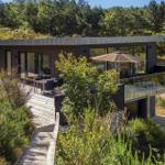 Moderne Villa mit Terrasse und Garten. Holzterrasse, Glasgeländer und Sonnenschirm.