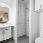 Badezimmer mit Dusche, Waschbecken und Toilette. Weiße Fliesen und Schränke.
