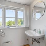 Badezimmer mit Waschbecken, Spiegel und Fenster mit Blick auf Grün.
