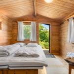 Ein Schlafzimmer mit Holzwänden, Bett und Fenster zum Garten.
