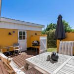 Terrasse mit Holztisch, Stühlen und Grill. Gelber Hauswänden und geschlossener Sonnenschirm.