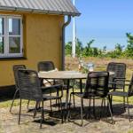 Außenbereich mit Tisch und Stühlen vor gelbem Haus mit Meerblick.
