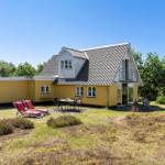 Ein gelbes Haus mit Terrasse und Liegestühlen in einer grünen Umgebung.