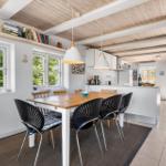 Essbereich mit Tisch und Stühlen. Küche mit Arbeitsplatte und Fenstern. Holzdecke und Bücherregal.
