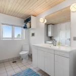 Badezimmer mit Waschbecken, Toilette und Fenster. Holzdecke und weiße Schränke.