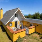 Ein gelbes Haus mit Terrasse und Meerblick. Weiße Fenster und grauer Dachfirst.
