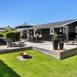 A holiday home with a large terrace, garden, and fire pit. Furniture and plants are arranged on the terrace.