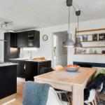 Kitchen with dining area, black cabinets, wooden table, and pendant lamps.