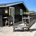 Deck with grill, table, chairs, and lounge chair in front of black wood house.