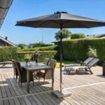 Deck with table, chairs, and umbrella. Background: green hedge and houses.
