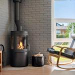 A wood-burning stove stands next to a chair by a window. A TV and a basket are also visible.