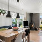 Dining room with wooden table, black pendant lights, and fireplace. Outside green area and seating.