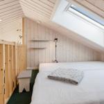 Schlafzimmer mit Dachfenster, Holzwand und Bett mit Decke.