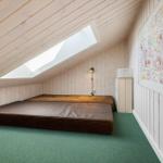 Zimmer mit Dachschrägen, Schlafcouch und großem Fenster. Wand mit Zeichnungen.