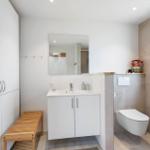 Badezimmer mit Waschbecken, Spiegel, Toilette und Holzbank.