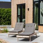 Zwei Liegestühle mit Kissen stehen auf einer Terrasse vor einem Holzhaus mit großen Fenstern.