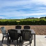 Terrasse mit Tisch und Stühlen, Blick auf grüne Hecke und Himmel.