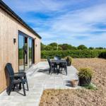 Terrasse mit Sitzgruppe neben Holzhaus. Hinterhof mit Beeten und Hecke.