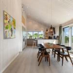 Essbereich mit Holztisch, Stühlen und Küchenbereich. Große Fenster und Wandbild.