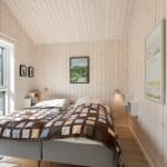 Schlafzimmer mit Holzwandverkleidung, Bett und Fenster zum Garten.
