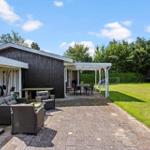 Hinterhof mit Terrasse, Gartenmöbeln und Spielplatz. Schwarze Hauswand und grüner Rasen.