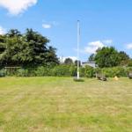 Großer Garten mit Spielplatz, Bänken und Feuerstelle unter blauem Himmel.