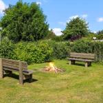 Garten mit Holzbank, Feuerstelle und grüner Hecke unter blauem Himmel.