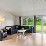 Wohnzimmer mit Sofa, Sessel und Glastür zur grünen Außenterrasse.