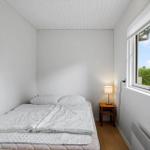 Ein Schlafzimmer mit Bett, Nachttisch und Lampe. Durch das Fenster ist ein Baum sichtbar.