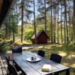Terrasse mit Tisch und Stühlen im Wald. Im Hintergrund steht eine rote Hütte.