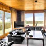Living room with black leather furniture, wooden ceiling, and large windows overlooking green areas.