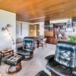 Living and dining area with leather sofa, chairs, and bookcase. Wooden ceiling and fireplace visible.